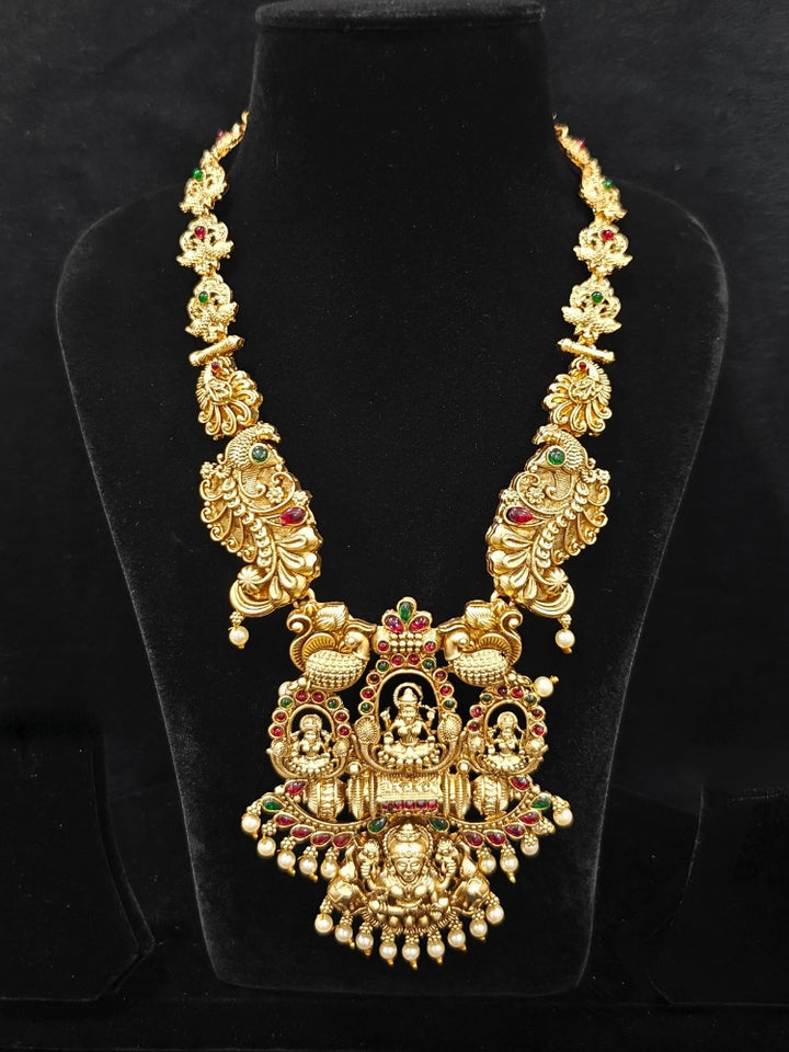The Kamakshi Temple Necklace Set featuring a traditional gold Long necklace and matching earrings with Goddess Laxmi in the middle, along with pink and green colored stones and pearls, Perfect Temple necklace set for weddings and festivals.