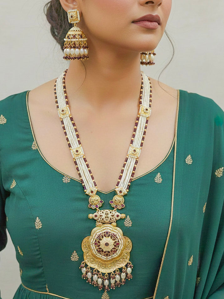 Close-up of a woman wearing an ornate traditional Purple Rajwadi gold Long jewellery set and earrings with Pearls, Crystal beads, American Diamonds, Colored Stones and Meenakari work.  Elegant Anarkali look paired with a traditional Rajwadi artificial necklace. Wedding guest styling a Rajwadi artificial necklace. 
