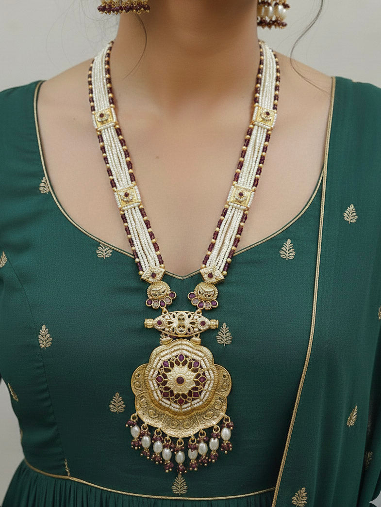 Close-up of a woman wearing an ornate traditional Purple Rajwadi gold Long jewellery set and earrings with Pearls, Crystal beads, American Diamonds, Colored Stones and Meenakari work.  Elegant Anarkali look paired with a traditional Rajwadi artificial necklace. Wedding guest styling a Rajwadi artificial necklace. 