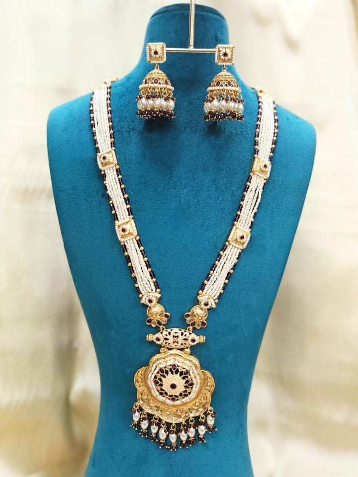Close-up of an ornate traditional Purple Rajwadi gold Long jewellery set and earrings with Pearls, Crystal beads, American Diamonds, Colored Stones and Meenakari work.  Elegant Anarkali look paired with a traditional Rajwadi artificial necklace. Wedding guest styling a Rajwadi artificial necklace. 