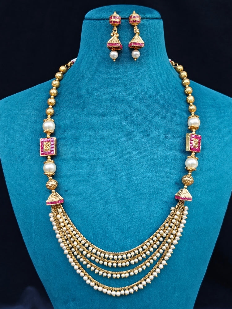 Close-up of an ornate traditional (Gold Polish) Long jewellery set and earrings with Pearls and Colored Stone. Mehendi function outfit styled with a lightweight Pearl necklace. Woman pairing a traditional Pearl necklace with a silk saree.
