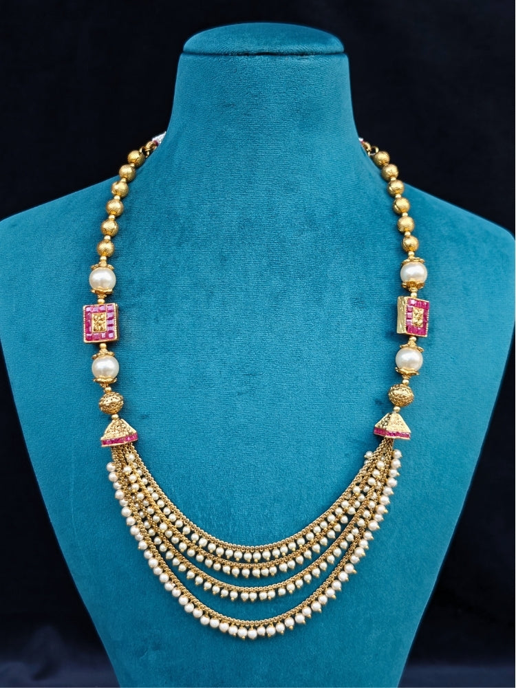 Close-up of an ornate traditional (Gold Polish) Long jewellery set and earrings with Pearls and Colored Stone. Mehendi function outfit styled with a lightweight Pearl necklace. Woman pairing a traditional Pearl necklace with a silk saree.