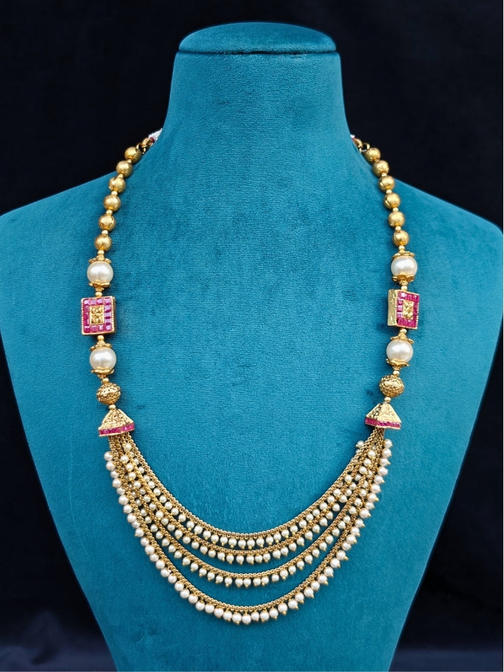 Close-up of an ornate traditional (Gold Polish) Long jewellery set and earrings with Pearls and Colored Stone. Mehendi function outfit styled with a lightweight Pearl necklace. Woman pairing a traditional Pearl necklace with a silk saree.