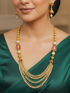 Close-up of a woman wearing an ornate traditional (Gold Polish) Long jewellery set and earrings with Pearls and Colored Stone. Mehendi function outfit styled with a lightweight Pearl necklace. Woman pairing a traditional Pearl necklace with a silk saree.