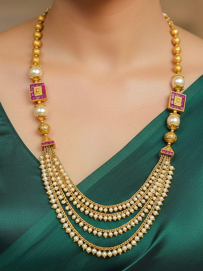 Close-up of a woman wearing an ornate traditional (Gold Polish) Long jewellery set and earrings with Pearls and Colored Stone. Mehendi function outfit styled with a lightweight Pearl necklace. Woman pairing a traditional Pearl necklace with a silk saree.