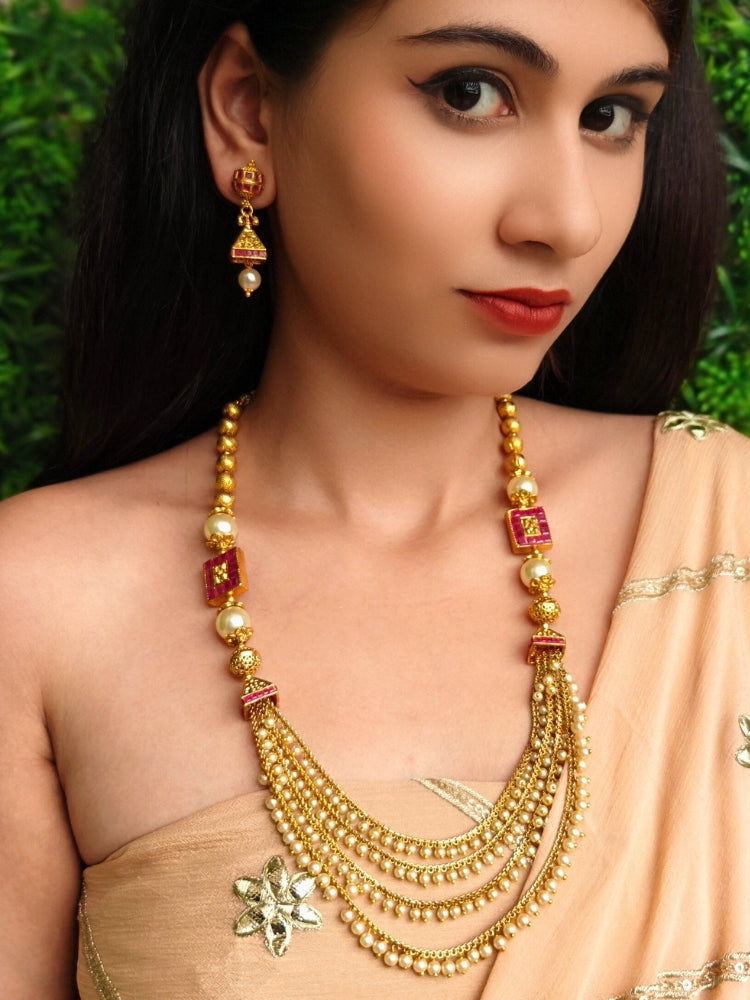 Close-up of a woman wearing an ornate traditional (Gold Polish) Long jewellery set and earrings with Pearls and Colored Stone. Mehendi function outfit styled with a lightweight Pearl necklace. Woman pairing a traditional Pearl necklace with a silk saree.