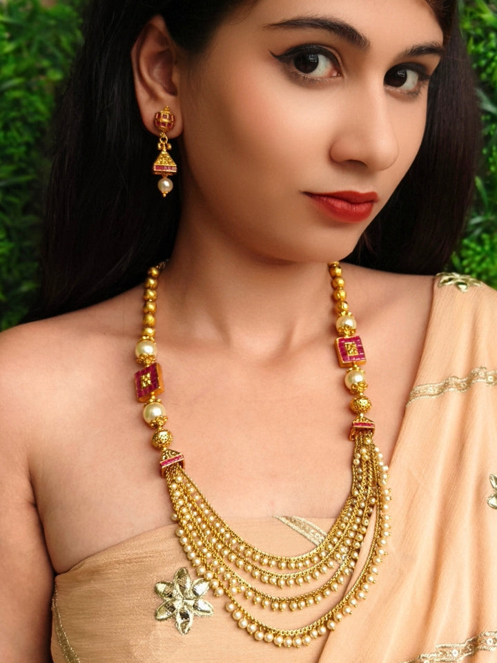 Close-up of a woman wearing an ornate traditional (Gold Polish) Long jewellery set and earrings with Pearls and Colored Stone. Mehendi function outfit styled with a lightweight Pearl necklace. Woman pairing a traditional Pearl necklace with a silk saree.