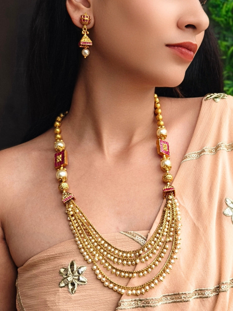 Close-up of a woman wearing an ornate traditional (Gold Polish) Long jewellery set and earrings with Pearls and Colored Stone. Mehendi function outfit styled with a lightweight Pearl necklace. Woman pairing a traditional Pearl necklace with a silk saree.