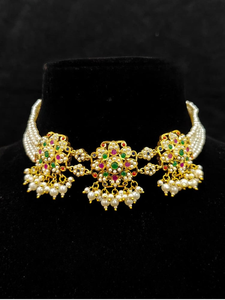 Close-up of an ornate traditional Navratan Choker jadau gold jewellery set and  jadau earrings with Pearl and Navratan Colored Stone. Festive celebration look featuring a Jadau artificial necklace. Close-up of intricate Jadau detailing in bridal jewelry.