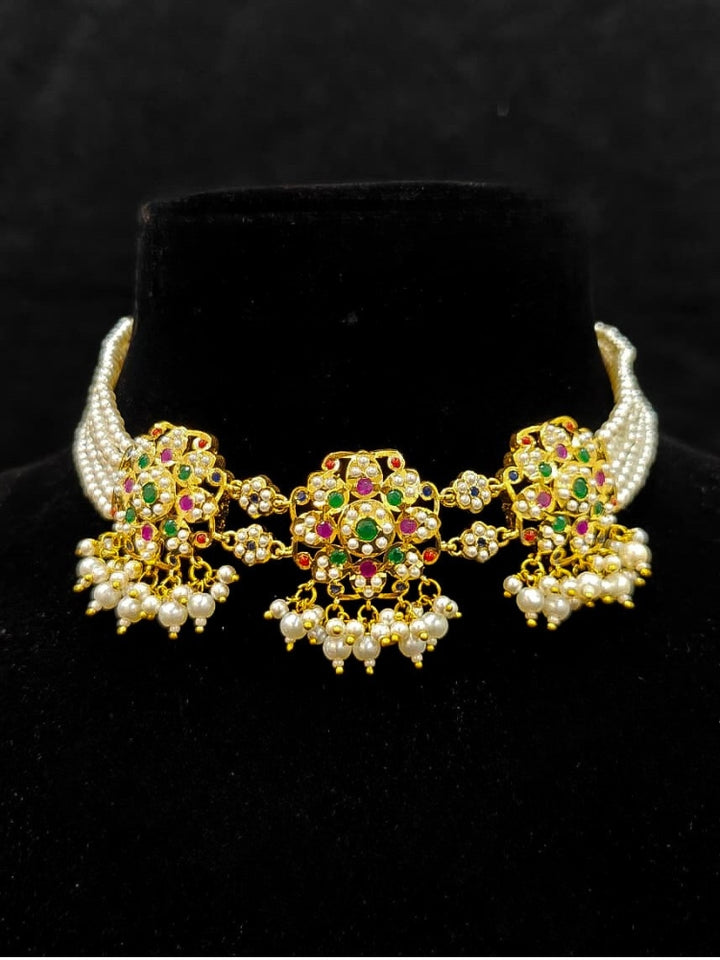 Close-up of an ornate traditional Navratan Choker jadau gold jewellery set and  jadau earrings with Pearl and Navratan Colored Stone. Festive celebration look featuring a Jadau artificial necklace. Close-up of intricate Jadau detailing in bridal jewelry.