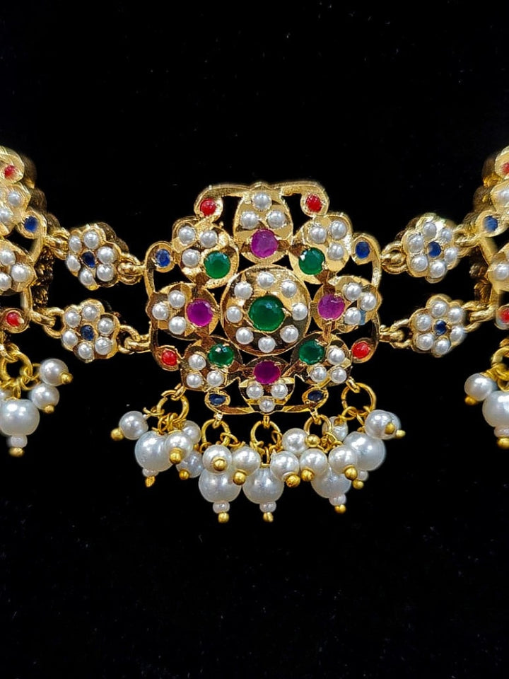 Close-up of an ornate traditional Navratan Choker jadau gold jewellery set and  jadau earrings with Pearl and Navratan Colored Stone. Festive celebration look featuring a Jadau artificial necklace. Close-up of intricate Jadau detailing in bridal jewelry.
