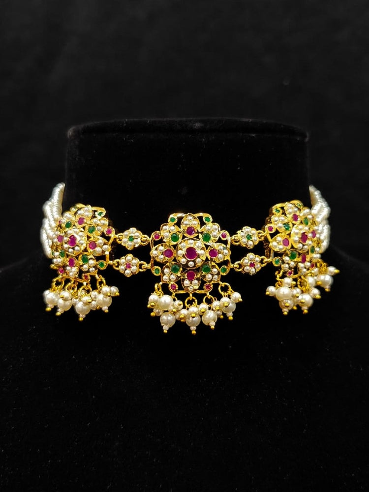 Close-up of an ornate traditional Ruby Pink and Green Choker jadau gold jewellery set and  jadau earrings with Pearl and Colored Stone. Festive look completed with a handcrafted Jadau necklace. A royal Jadau necklace for festive events in India.