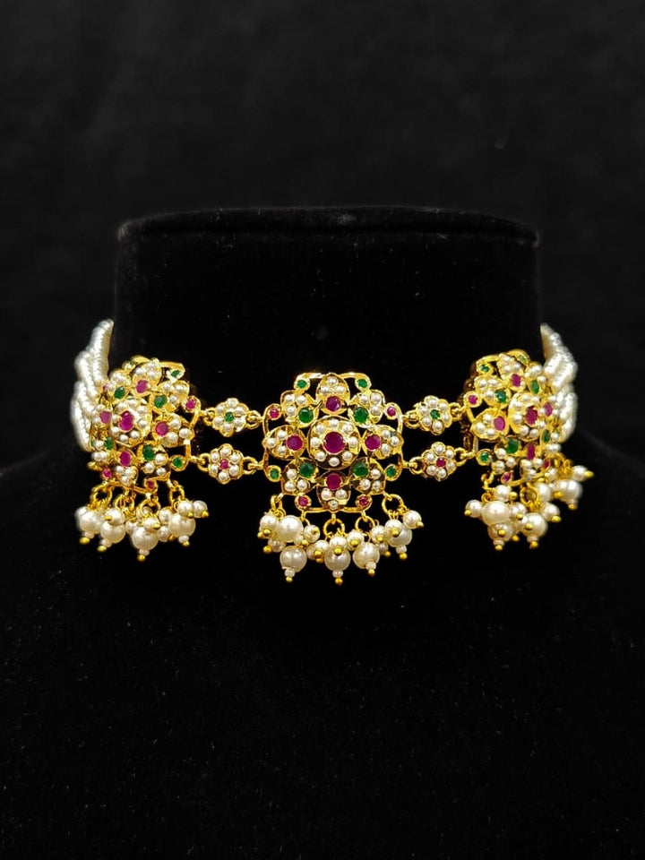 Close-up of an ornate traditional Ruby Pink and Green Choker jadau gold jewellery set and  jadau earrings with Pearl and Colored Stone. Festive look completed with a handcrafted Jadau necklace. A royal Jadau necklace for festive events in India.