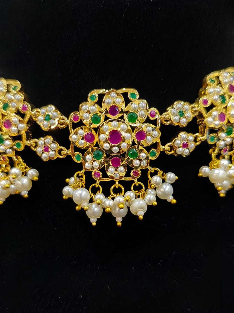 Close-up of an ornate traditional Ruby Pink and Green Choker jadau gold jewellery set and  jadau earrings with Pearl and Colored Stone. Festive look completed with a handcrafted Jadau necklace. A royal Jadau necklace for festive events in India.