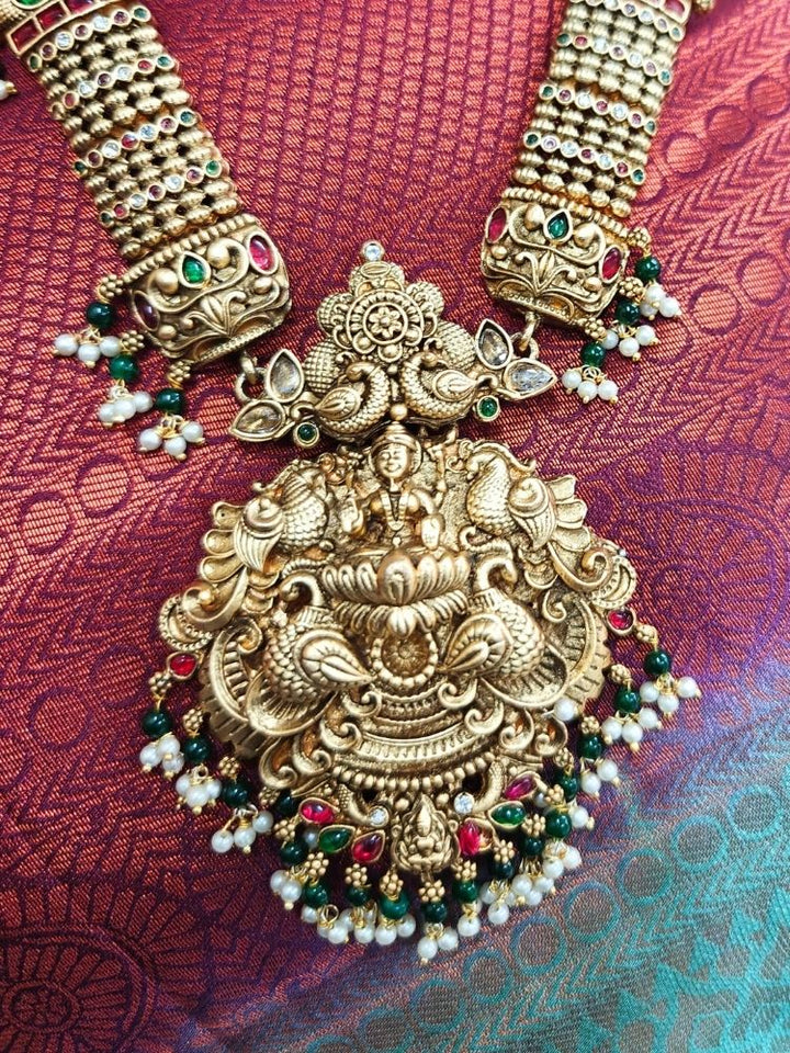 A woman wearing a rich maroon and gold saree, adorned with the Kantha Temple Necklace Set featuring intricate detailed design of  Maa Laxmi, matching wedding accessories, and elegant gold jhumka earrings.