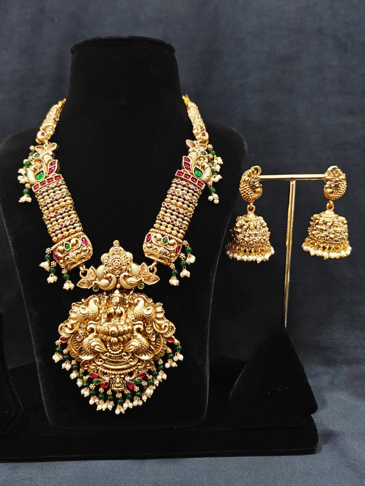 the Kantha Temple Necklace Set featuring a traditional gold Long necklace and matching earrings with Goddess Laxmi in the middle, along with pink and green colored stones, paired with Saree —Bride showcasing a premium temple artificial jewelry set for wedding rituals.