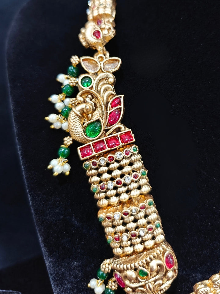 the Kantha Temple Necklace Set featuring a traditional gold Long necklace and matching earrings with Goddess Laxmi in the middle, along with pink and green colored stones, paired with Saree —Bride showcasing a premium temple artificial jewelry set for wedding rituals.