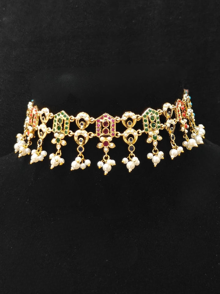 Close-up of an ornate traditional Navratan jadau gold jewellery set and jadau earrings with navratan color stone and Pearls. Elegant reception look featuring a luxury Jadau artificial jewelry set. Festive celebration look featuring a Jadau artificial necklace.