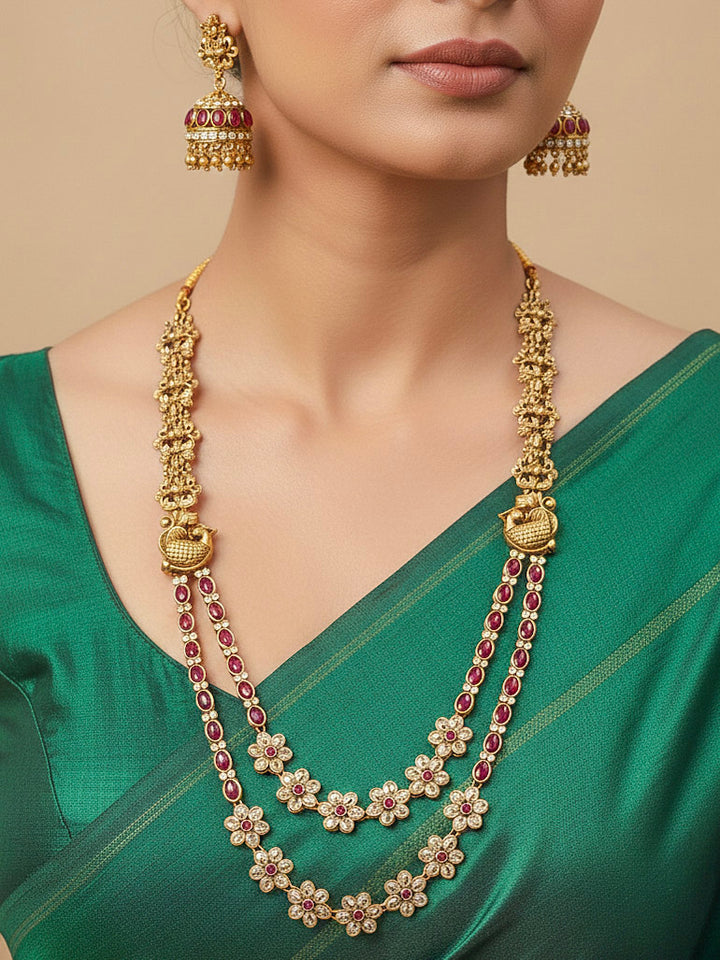 A woman wearing the Red Karuna Temple Necklace Set featuring a traditional gold Long necklace and matching earrings with Red colored stones, paired with a Saree—Saree look enhanced with a royal temple imitation necklace.