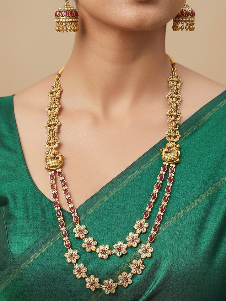 A woman wearing the Red Karuna Temple Necklace Set featuring a traditional gold Long necklace and matching earrings with Red colored stones, paired with a Saree—Saree look enhanced with a royal temple imitation necklace.