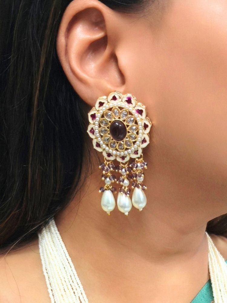 A woman wears the Kashish Necklace Set— A necklace with multiple strands of white pearls and pink crystal stones, with a big pendant made with enamel meenakari work, kundan detailing and an oval pink-purple stone in the middle, along with pearls and other crystals hanging at the bottom. Only her lower face and upper torso are shown; she’s dressed in a green and gold saree. Close-up of enamel work in Meenakari artificial wedding jewelry.
