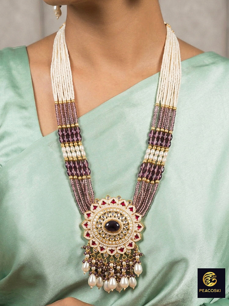Close-up of a woman wearing an ornate traditional Lilac Rajwadi gold Long jewellery set and earrings with Pearls, Crystal beads, Tumble stones, American Diamonds, Colored Stones, Meenakari work and Pearls. Festive Diwali outfit enhanced with a Rajwadi artificial necklace. Woman wearing a bridal Rajwadi necklace for a reception function. Close-up of enamel work in Meenakari artificial wedding jewelry.