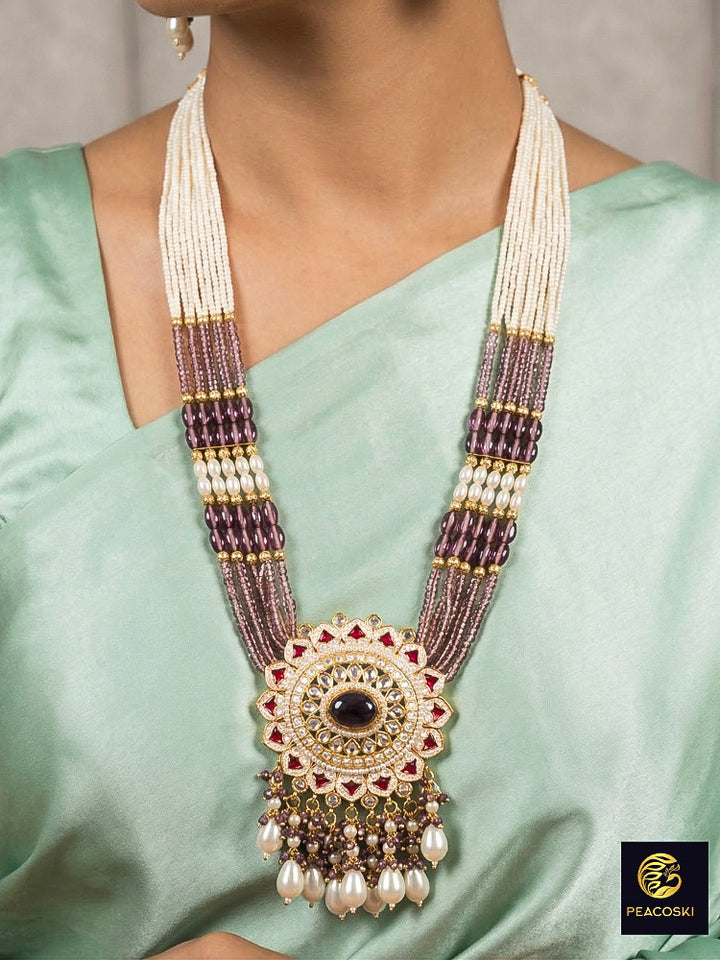 Close-up of a woman wearing an ornate traditional Lilac Rajwadi gold Long jewellery set and earrings with Pearls, Crystal beads, Tumble stones, American Diamonds, Colored Stones, Meenakari work and Pearls. Festive Diwali outfit enhanced with a Rajwadi artificial necklace. Woman wearing a bridal Rajwadi necklace for a reception function. Close-up of enamel work in Meenakari artificial wedding jewelry.
