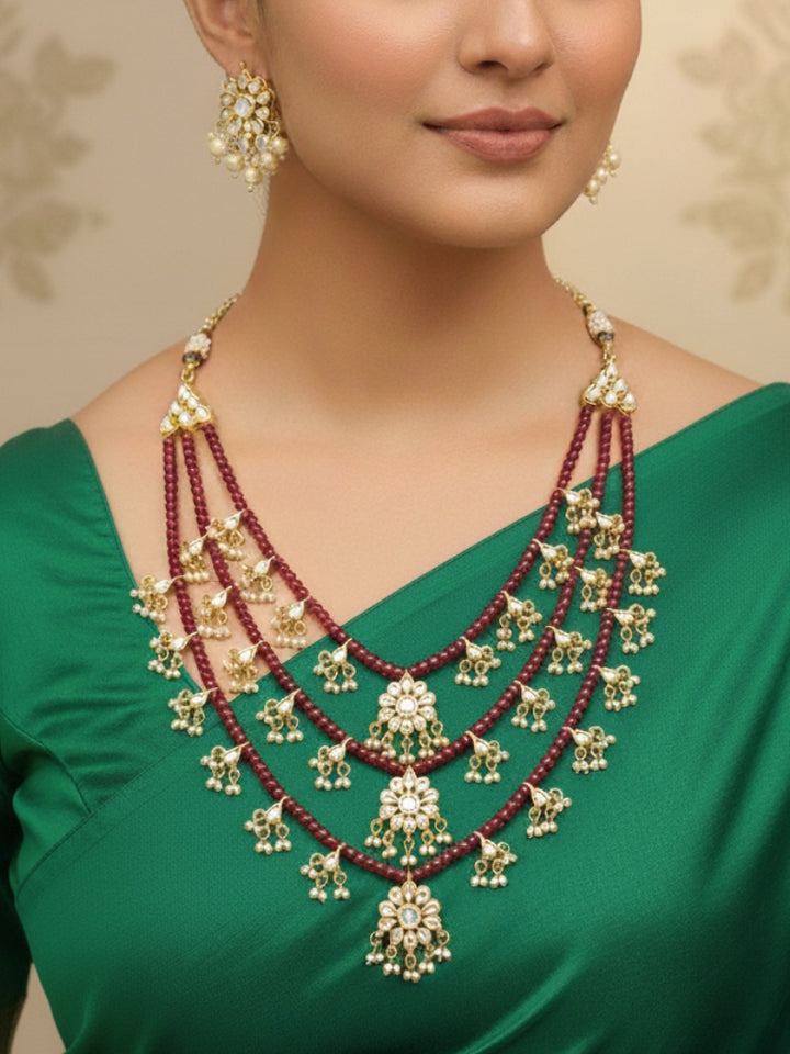 Close-up of a woman wearing an ornate traditional Maroon Layered jewellery set and earrings with Kundan and Beads. Wedding guest wearing a lightweight Kundan necklace for a festive function. Saree look completed with a traditional artificial Kundan set.