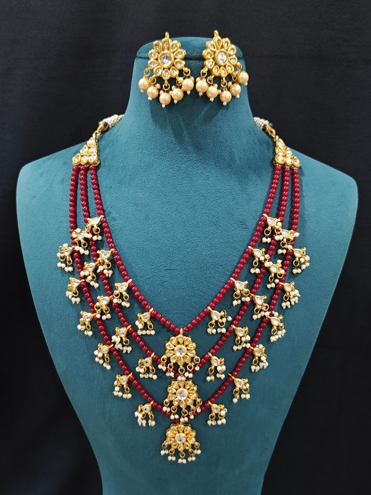 Close-up of an ornate traditional Maroon Layered jewellery set and earrings with Kundan and Beads. Wedding guest wearing a lightweight Kundan necklace for a festive function. Saree look completed with a traditional artificial Kundan set.