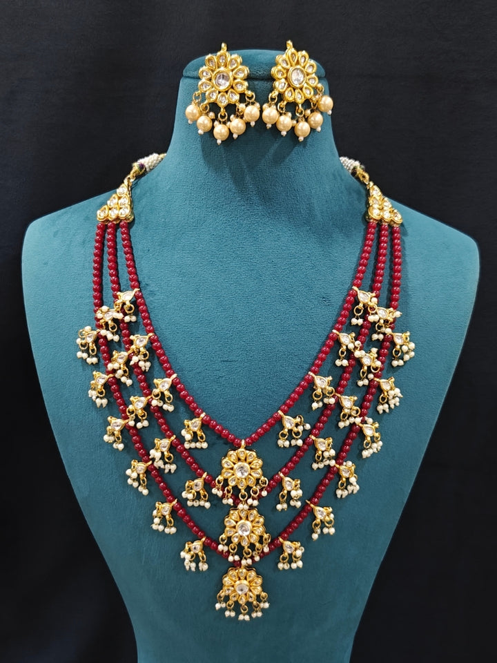Close-up of an ornate traditional Maroon Layered jewellery set and earrings with Kundan and Beads. Wedding guest wearing a lightweight Kundan necklace for a festive function. Saree look completed with a traditional artificial Kundan set.