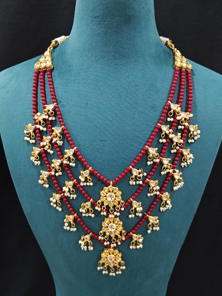 Close-up of an ornate traditional Maroon Layered jewellery set and earrings with Kundan and Beads. Wedding guest wearing a lightweight Kundan necklace for a festive function. Saree look completed with a traditional artificial Kundan set.