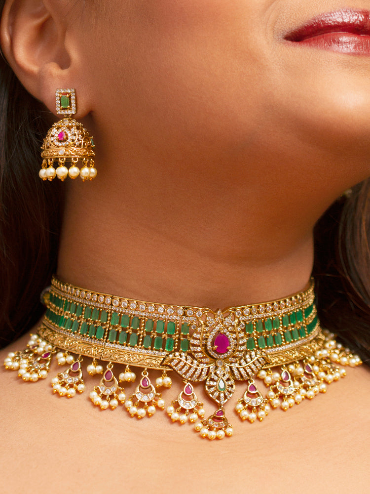 A close-up of a woman wearing the Kavira Choker Necklace Set—a green and pink necklace with gold details, green enamel, pink stones, pearl drops—paired with party earrings featuring pearls and a green gem.
