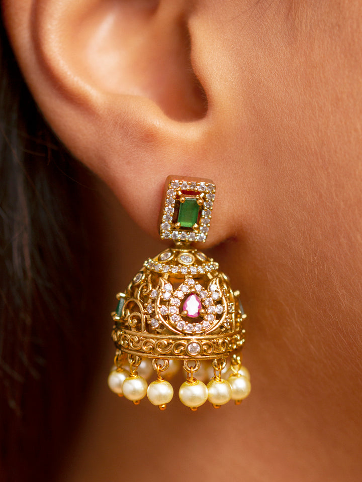 A close-up of a woman wearing the Kavira Choker Necklace Set—a green and pink necklace with gold details, green enamel, pink stones, pearl drops—paired with party earrings featuring pearls and a green gem.
