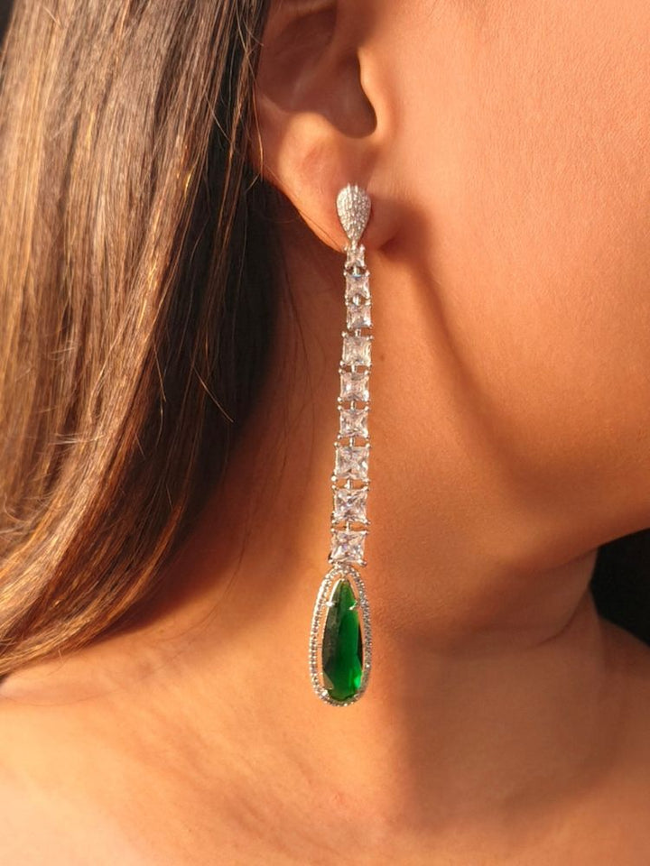 A woman wears the Kendall Green Earrings—long and elegant, set with four square American Diamonds and finished with a bold teardrop Green stone—ideal for enhancing a cocktail gown. American Diamond Cocktail Earrings, American Diamond Earring. 