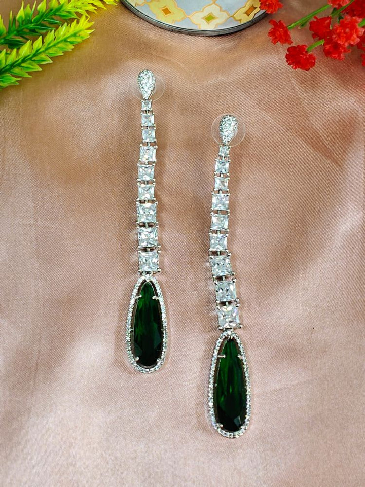 Kendall Red Earrings—long and elegant, set with four square American Diamonds and finished with a bold teardrop red stone—ideal for enhancing a cocktail gown. Set on a Peach background. American Diamond Cocktail Earrings, American Diamond Earring. 