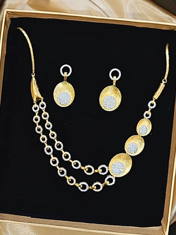 The Kensington Necklace Set is displayed in a box with a gold necklace featuring circular gold and silver accents, sparkling American Diamonds, and matching earrings—all set on black velvet with a satin gold border, perfect for parties.