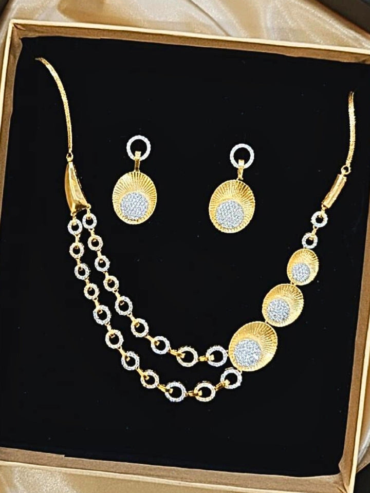 The Kensington Necklace Set is displayed in a box with a gold necklace featuring circular gold and silver accents, sparkling American Diamonds, and matching earrings—all set on black velvet with a satin gold border, perfect for parties.