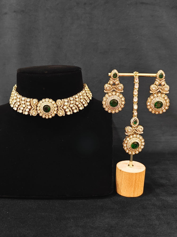 Close-up of an ornate traditional Green Diamond gold Polish Choker jewellery set and earrings and maangtikka with American Diamond and Green Colored Stones. A luxury American diamond necklace set styled beautifully for a wedding guest look in India. Mehendi function outfit styled with a lightweight American Diamond Necklace.