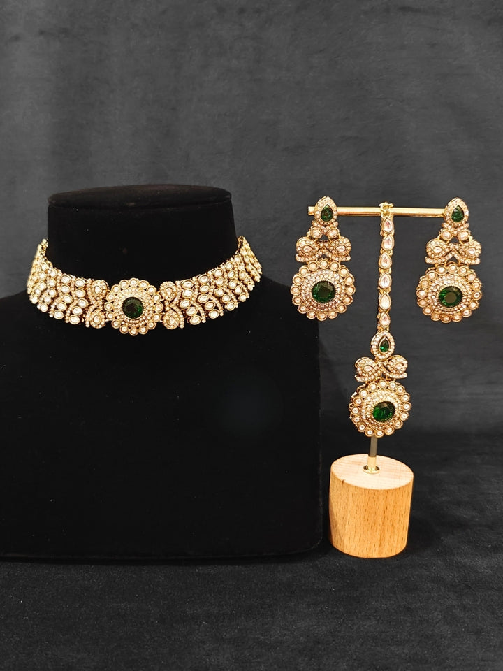 Close-up of an ornate traditional Green Diamond gold Polish Choker jewellery set and earrings and maangtikka with American Diamond and Green Colored Stones. A luxury American diamond necklace set styled beautifully for a wedding guest look in India. Mehendi function outfit styled with a lightweight American Diamond Necklace.