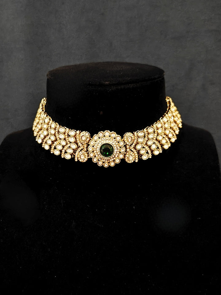 Close-up of an ornate traditional Green Diamond gold Polish Choker jewellery set and earrings and maangtikka with American Diamond and Green Colored Stones. A luxury American diamond necklace set styled beautifully for a wedding guest look in India. Mehendi function outfit styled with a lightweight American Diamond Necklace.