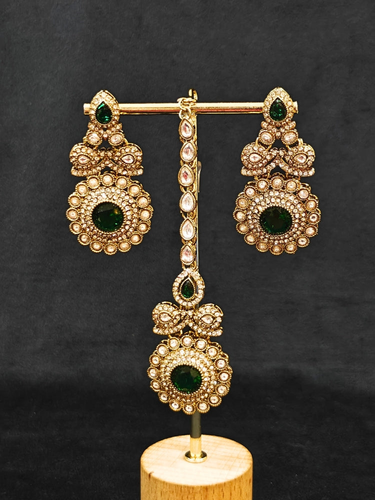 Close-up of an ornate traditional Green Diamond gold Polish Choker jewellery set and earrings and maangtikka with American Diamond and Green Colored Stones. A luxury American diamond necklace set styled beautifully for a wedding guest look in India. Mehendi function outfit styled with a lightweight American Diamond Necklace.