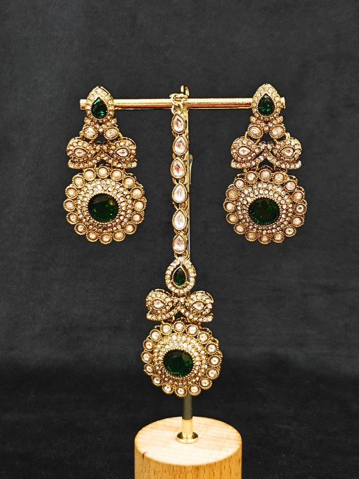 Close-up of an ornate traditional Green Diamond gold Polish Choker jewellery set and earrings and maangtikka with American Diamond and Green Colored Stones. A luxury American diamond necklace set styled beautifully for a wedding guest look in India. Mehendi function outfit styled with a lightweight American Diamond Necklace.