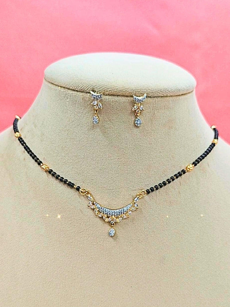 Kridha Mangalsutra—a gold necklace with black mangalsutra beads and matching earrings, pendant featuring sparkling American Diamonds—set against a cream dummy, perfect for your wedding ceremony dress. Diamond mangalsutra. Modern mangalsutra. 