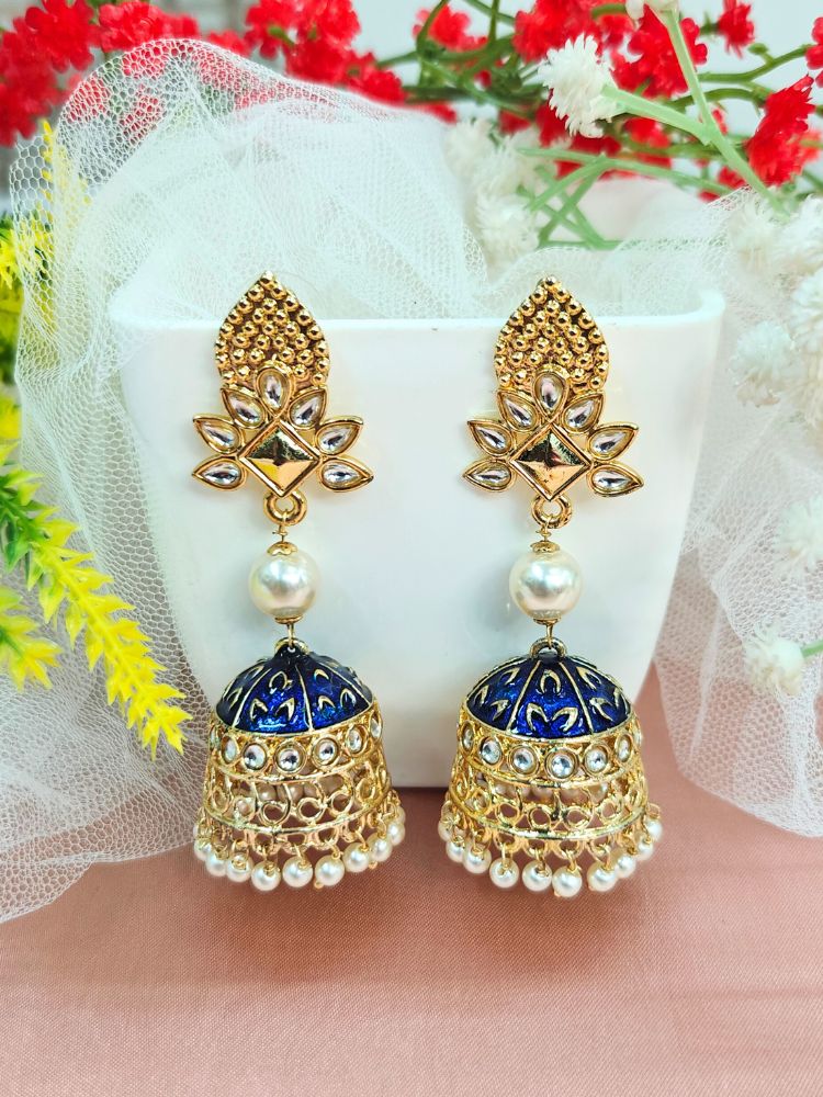 A close-up of a womans ear adorned with Kritika Black Earrings—large gold jhumkas featuring green meenakari work, pearl accents, kundan detailing, and a delicate floral moti near the earlobe.