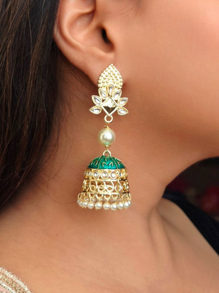 A close-up of a womans ear adorned with Kritika Green Earrings—large gold jhumkas featuring green meenakari work, pearl accents, kundan detailing, and a delicate floral motif near the earlobe.