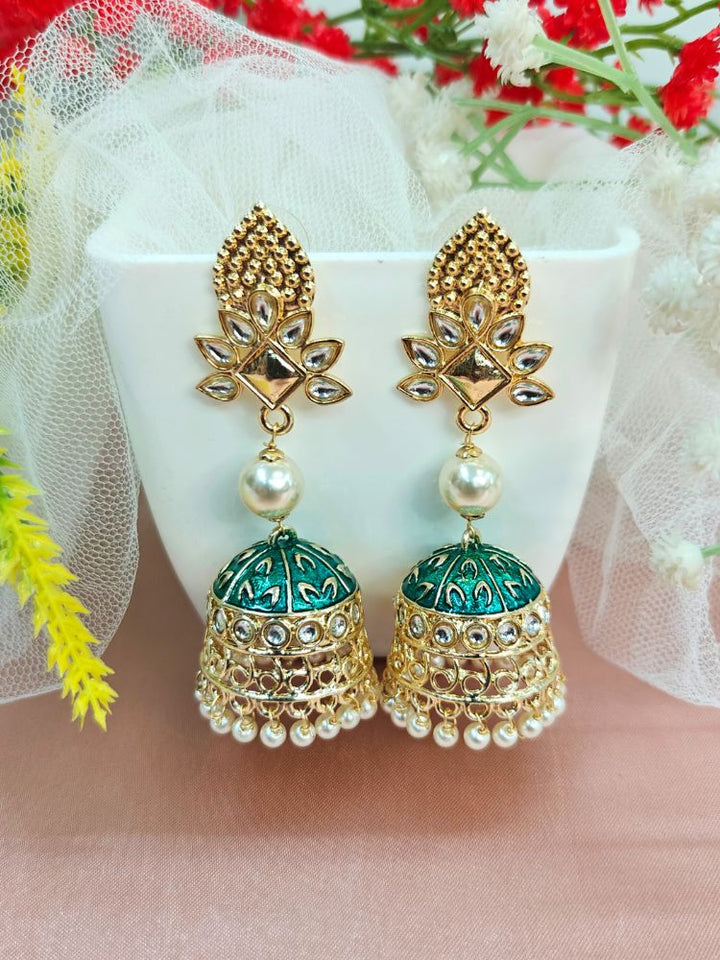 A close-up of a womans ear adorned with Kritika Black Earrings—large gold jhumkas featuring green meenakari work, pearl accents, kundan detailing, and a delicate floral moti near the earlobe.