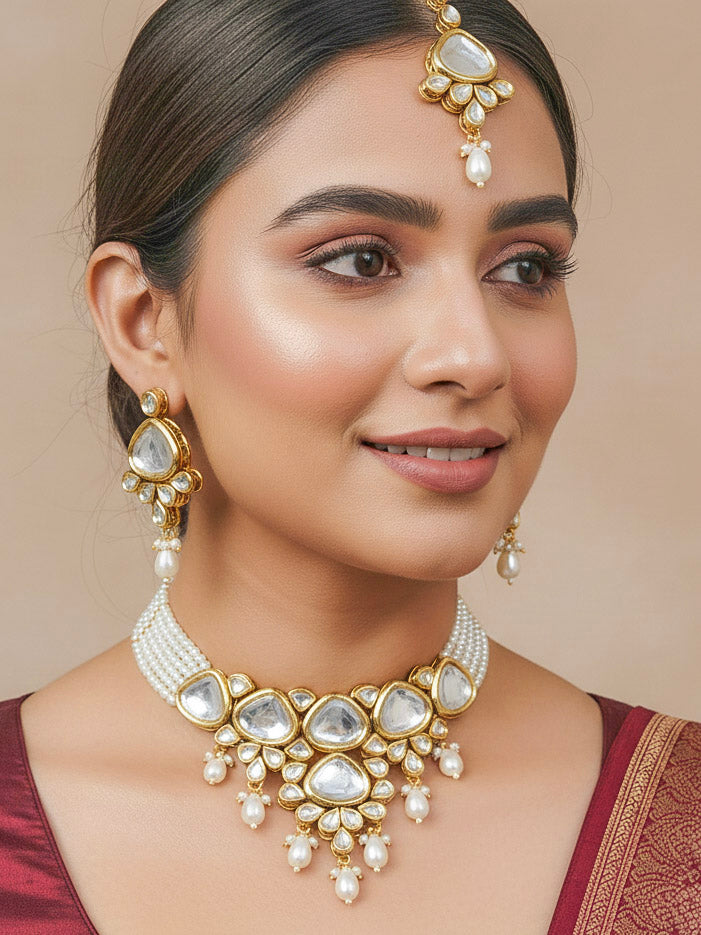 Close-up of a woman wearing an ornate traditional (Gold Polish) White Kundan Collar jewellery set and earrings and maangtikka with Pearls and Kundan. Wedding celebration look enhanced with a Kundan necklace. Mehendi ceremony look completed with a handcrafted Kundan jewelry set. Festive saree styling with a premium artificial Kundan necklace.