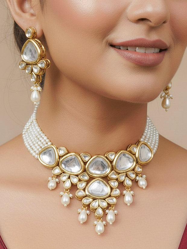 Close-up of a woman wearing an ornate traditional (Gold Polish) White Kundan Collar jewellery set and earrings and maangtikka with Pearls and Kundan. Wedding celebration look enhanced with a Kundan necklace. Mehendi ceremony look completed with a handcrafted Kundan jewelry set. Festive saree styling with a premium artificial Kundan necklace.