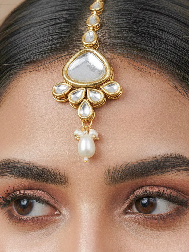 Close-up of a woman wearing an ornate traditional (Gold Polish) White Kundan Collar jewellery set and earrings and maangtikka with Pearls and Kundan. Wedding celebration look enhanced with a Kundan necklace. Mehendi ceremony look completed with a handcrafted Kundan jewelry set. Festive saree styling with a premium artificial Kundan necklace.