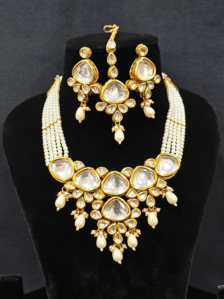 Close-up of an ornate traditional (Gold Polish) White Kundan Collar jewellery set and earrings and maangtikka with Pearls and Kundan. Wedding celebration look enhanced with a Kundan necklace. Mehendi ceremony look completed with a handcrafted Kundan jewelry set. Festive saree styling with a premium artificial Kundan necklace.